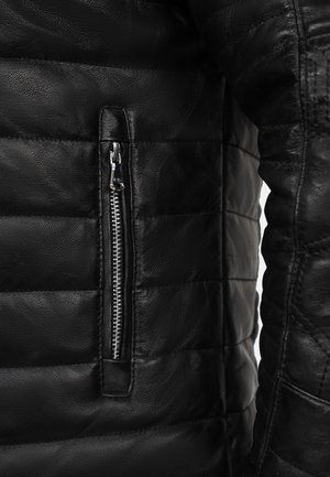 Veste en cuir noir avec texture matelassée, poche zippée verticale et finition lisse sur les manches. Design durable et ajusté.