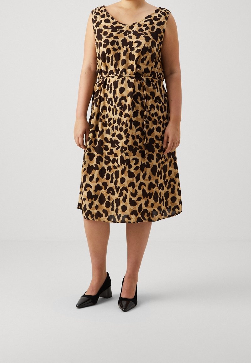 Vestido de estampado de leopardo en tonos marrón claro y marrón oscuro, sin mangas, con escote en v, cintura ceñida y falda fluida. Combinado con tacones negros de punta.
