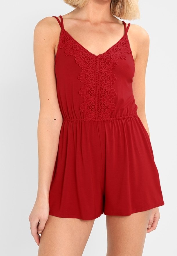 Röd rompers med spetskant längs halsen, tunna axelremmar och elastisk midja. Tillverkad av mjukt, lätt material med en avslappnad passform.