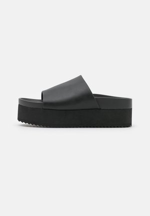Zwarte platform slip-on sandalen met een gladleren bovenkant, open teen en een dikke ribbelzool voor grip. Eenvoudig, minimalistisch ontwerp.