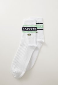 Witte katoenen sokken met een geribbelde structuur, marineblauwe en mintgroene strepen, en het "LACOSTE"-logo met een klein krokodillenembleem.