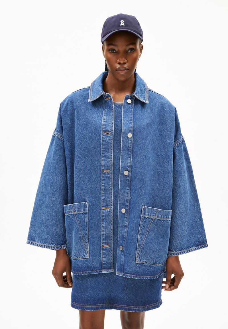 Oversized denim jacket in medium blue, featuring a collared neckline, button closure, two front pockets, and contrasting stitching details.