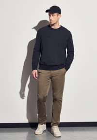 Merino neulepaita, khaki chinot ja kermaiset urheilukengät. Asusteessa on yksinkertainen muotoilu, jossa on rento malli ja minimaalinen varusteiden käyttö.