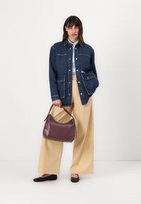 Jachetă din denim cu două buzunare frontale, cămașă albă, pantaloni bej cu picior larg, pantofi negri și o geantă din piele burgundy.