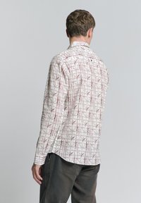 Lange mouwenshirt van lichte stof, met een witte basis en een rood ruitpatroon. De achterkant heeft een knoopdetail bij de kraag.