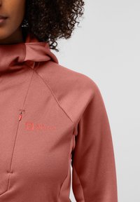 Rosa Fleece-Hoodie mit hohem Kragen, sichtbarem Reißverschlussfach, strukturiertem Stoff und einem Logo auf der Brust.