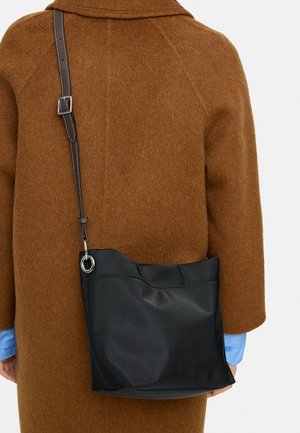 Brązowy wełniany płaszcz noszony na jasnoniebieskiej koszuli, z czarną skórzaną torbą na ramię zawieszoną na ciemnobrązowym pasku na plecach.