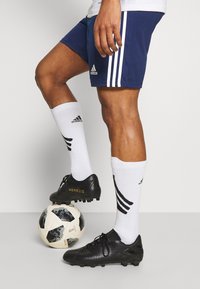 Black soccer cleats with textured surface, white socks with black stripes, navy shorts with white stripes, and a patterned soccer ball.