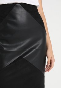 Schwarzer Rock aus einer Kombination von mattem Wildleder und glänzendem Leder, mit einem geometrischen Design und diagonalen Akzentdetails.