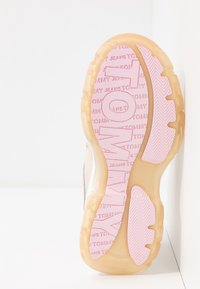 La suola delle scarpe presenta un materiale traslucido di un marrone chiaro testurizzato con un branding rosa evidente e un motivo a spina di pesce per la trazione.