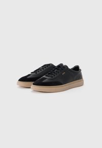 Zwarte leren en suède sneakers met een gestructureerd oppervlak, beige rubberen zool, ronde neus en zwarte veters, met een logo op de zijkant.