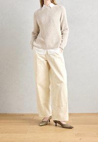Pull en maille beige, chemise blanche à col en dessous, pantalon large crème, et escarpins dorés à bout pointu. Design simple, texture douce, et couleurs neutres.