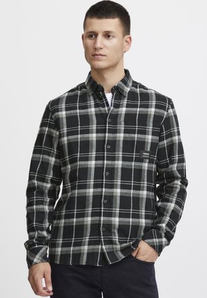 Camisa de cuadros en blanco y negro con botones y mangas largas, la textura de la tela es suave y tejida, con una pequeña etiqueta de marca en el pecho.