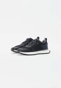 Zwarte sport schoenen van mesh en synthetisch materiaal, rubberen zool, witte tussenzool en een blauw accentdetail aan de zijkant.