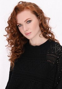 Un pull en tricot noir avec un motif ajouré complexe, un col rond et des manches longues avec des motifs texturés.