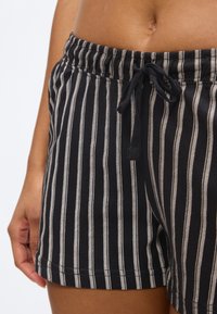 Μέση και άνω μηρός ατόμου που φοράει μαύρα σορτς με κάθετες λευκές ρίγες και δεμένο κορδόνι στη μέση.