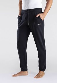 Black jogger pants made of soft fabric, featuring an elastic waistband with drawstring, side pockets, and a small white logo on the left side.