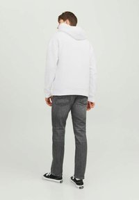 Sweatshirt blanc avec une grande capuche, associé à un jean gris et des baskets noires. Le tissu semble lisse, avec des poignets et un ourlet côtelés.