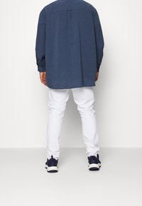 Codzienny strój składający się z ciemnoniebieskiej koszuli z długim rękawem, białych spodni i granatowych tenisówek. Koszula ma mankiety na guziki i tylny karczek.