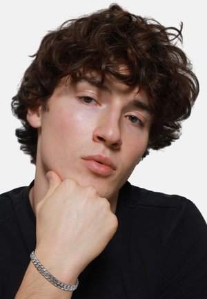 Silver chain bracelet on wrist, featuring interlocking links. Close-up of a male model resting chin on hand, wearing a black shirt.