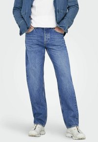 Vaqueros de denim de color azul claro con un diseño de pierna recta, que presentan costuras en contraste y un estilo clásico de cinco bolsillos. Llevados con una camiseta blanca.