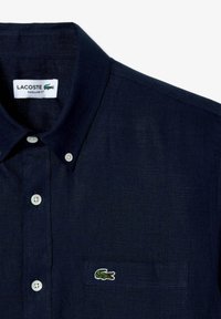 Marineblauw collared shirt met knoopsluiting, gemaakt van textuurstof. Voorzien van een zak op de linkerkant van de borst en een geborduurd krokodillenlogo.