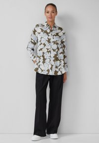 Camicia a maniche lunghe a bottoni in verde oliva scuro con fiori blu e bianchi, abbinata a pantaloni neri e scarpe bianche. Dotata di tasche laterali.