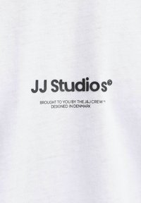 Camiseta de algodón blanca con texto impreso en negro: "JJ Studios," "traído a ti por el equipo J&J," y "diseñado en Dinamarca."
