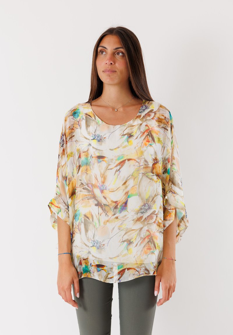 Blusa leggera con motivo floreale, scollatura a barca, maniche a tre quarti e vestibilità ampia. I colori includono crema, giallo e accenti verdi.