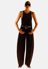 Jumpsuit nero senza maniche con un corpetto aderente e pantaloni a gamba larga, accentuato da una cintura metallica argentea e occhiali da sole eleganti.