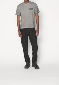 Szara koszulka z krótkim rękawem z nadrukiem "N°21" w kolorze czarnym, w komplecie z czarnymi spodniami i czarnymi butami sportowymi, stojąca na białym tle.
