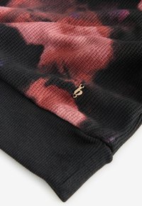 Black textured fabric with a pink and purple tie-dye pattern, featuring a small gold logo accent on the hem.