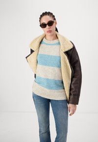 Brown leather jacket with shearling collar, beige and blue striped fuzzy sweater, and blue jeans. Dark sunglasses complete the look.