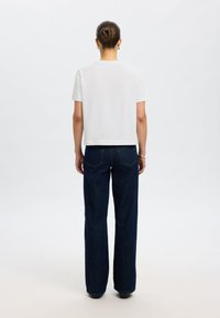 Wit t-shirt met korte mouwen en een rechte zoom, gecombineerd met hooggetailleerde, wijd uitlopende donkerblauwe jeans. Eenvoudig ontwerp, zonder zichtbare patronen.