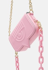 Pink crossbody bag with embossed eye design, gold chain strap, and chunky pink plastic chain links hanging against a white background.