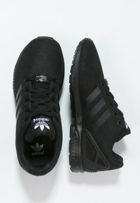 Black Adidas sneakers with a textured mesh upper, three parallel stripes, and a cushioned sole. Features a lace-up design and logo accents.