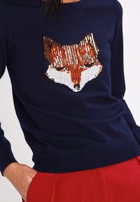 Mörkblå tröja med en rävdesign av paljetter framtill. Räven har nyanser av orange, vitt och brunt med skinande texturer.