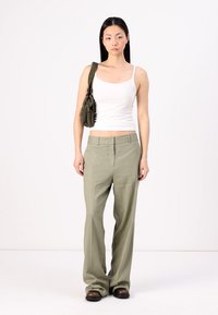 Top corto bianco, pantaloni ampi verde oliva e mocassini scuri. La modella porta una piccola borsa testurizzata verde oliva. Sfondo semplice.