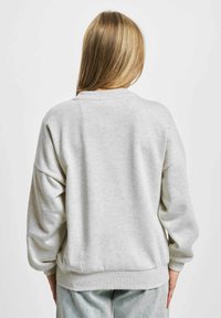 Lys grå sweatshirt med rund hals, nedre skuldre og ribbede mansjetter. Myk tekstur, med rett kant ved livet.