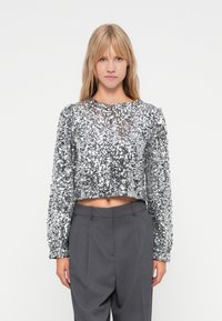 Strieborný trblietajúci sa crop top s okrúhlym v�ýstrihom a dlhými rukávmi, skombinovaný s vysokokoštovými sivými nohavicami. Po celé ploche má lesklú textúru.