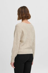 Beige neulepaita, jossa on rento malli, ribbineuleiset hihat ja helma, pyöreä kaula-aukko ja hienovaraisia sävyjä kauttaaltaan.
