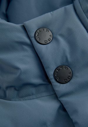Zbliżenie niebieskiego materiału izolacyjnego z czarnymi zatrzaskami z wytłoczonym napisem, ukazujące gładką teksturę i szczegó�ły w szwie.