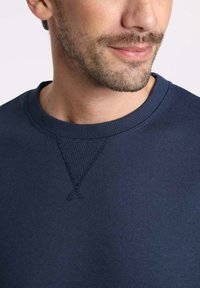 Sweat-shirt bleu marine avec un col côtelé et des détails en tricot triangulaires au niveau du col. Texture lisse avec des accents de couture minimalistes.