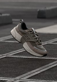 Leichter Sneaker mit einem Obermaterial aus braunem Wildleder und Mesh, grauen Akzenten, strukturierten Sohle und Schnürsystem, das für Komfort und Unterstützung konzipiert ist.