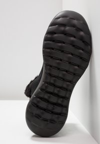 Semelle en caoutchouc noire avec surface texturée et motif en zigzag, présentant un bord lisse. La semelle a une légère courbe et une marque minimale visible.