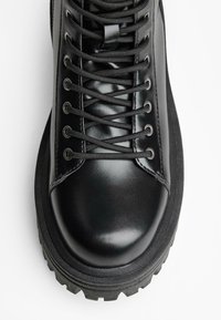 Černá kožená bota se zaoblenou špičkou, vybavená kovovými očky a černými šňůrami. Texturovaná podrážka s výrazným vzorem pro lepší přilnavost.