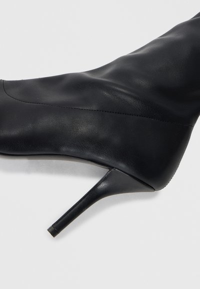 Melnas ādas augstpapēžu zābaki ar gludu faktūru, asu pirkstu un šauru stiletto papēdi. Satur minimālas šuves detaļas.