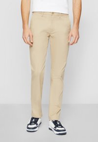 Chinos beige clair en coton lisse. Présentent une coupe droite, des poches latérales et une fermeture à un bouton à la taille.
