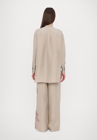 Camicia oversize beige chiaro con silhouette dritta e maniche lunghe, abbinata a pantaloni a gamba larga con una sottile stampa di palme.