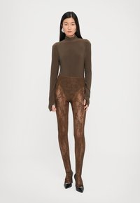 Brun langermet topp kombinert med gjennomsiktige brune leggings med blomstermønster. Outfitten er akkompagnert av spisse svarte hæler.